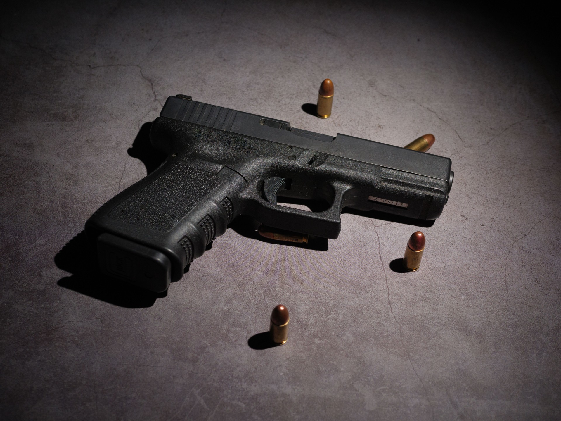 Close-up of a black metal 9mm automatic pistol with bullets all placed on a cement table with a black background.