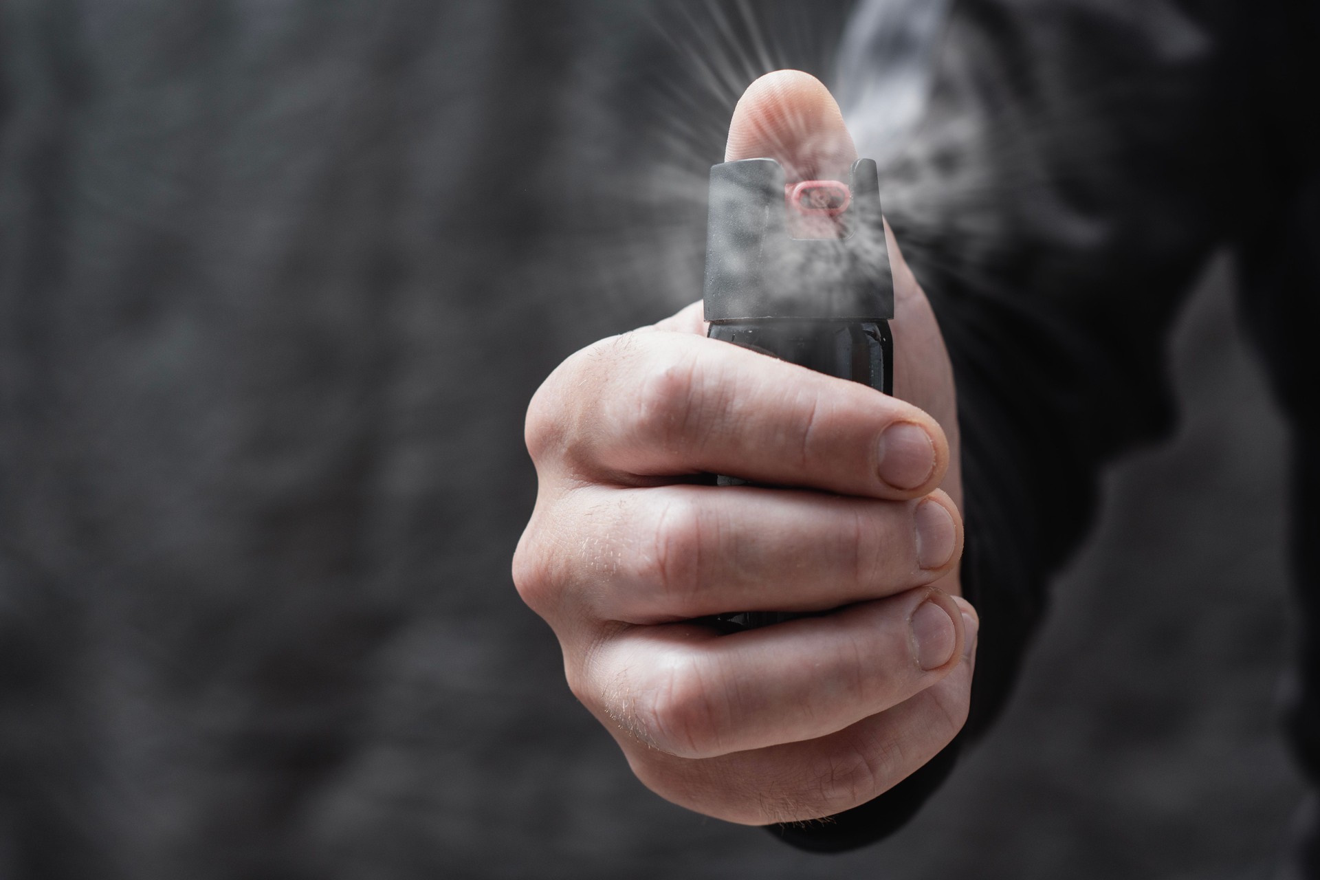 Close-up of a man hand pressing a pepper spray canister with visible aerosol release. Concept self-defense, protection, danger prevention, and personal safety.